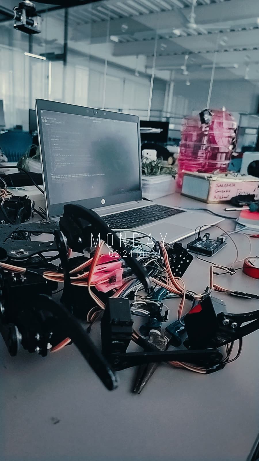Hexapod on a lab desk beside a laptop running code.